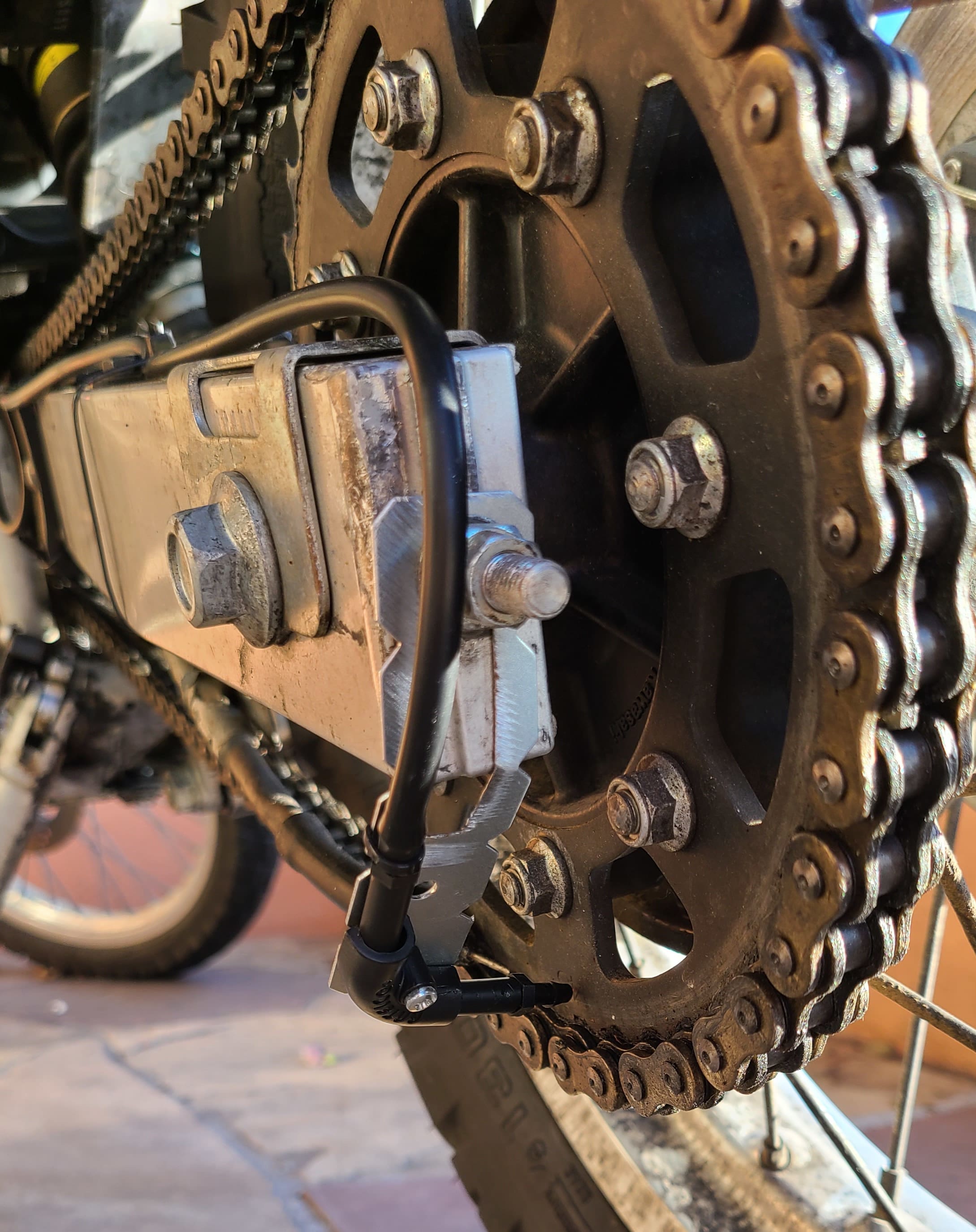 metal bracket keeping hose and nozzle in position on a rear motorcycle sprocket 